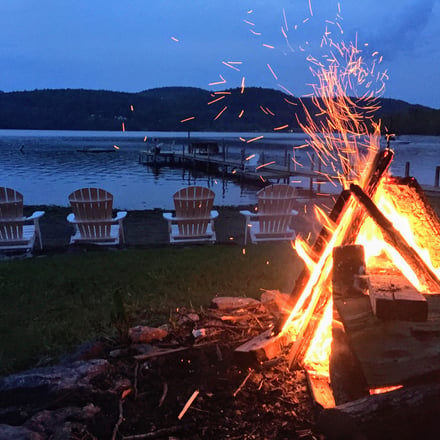 Lakeside bonfire with Adirondack chairs at dusk
